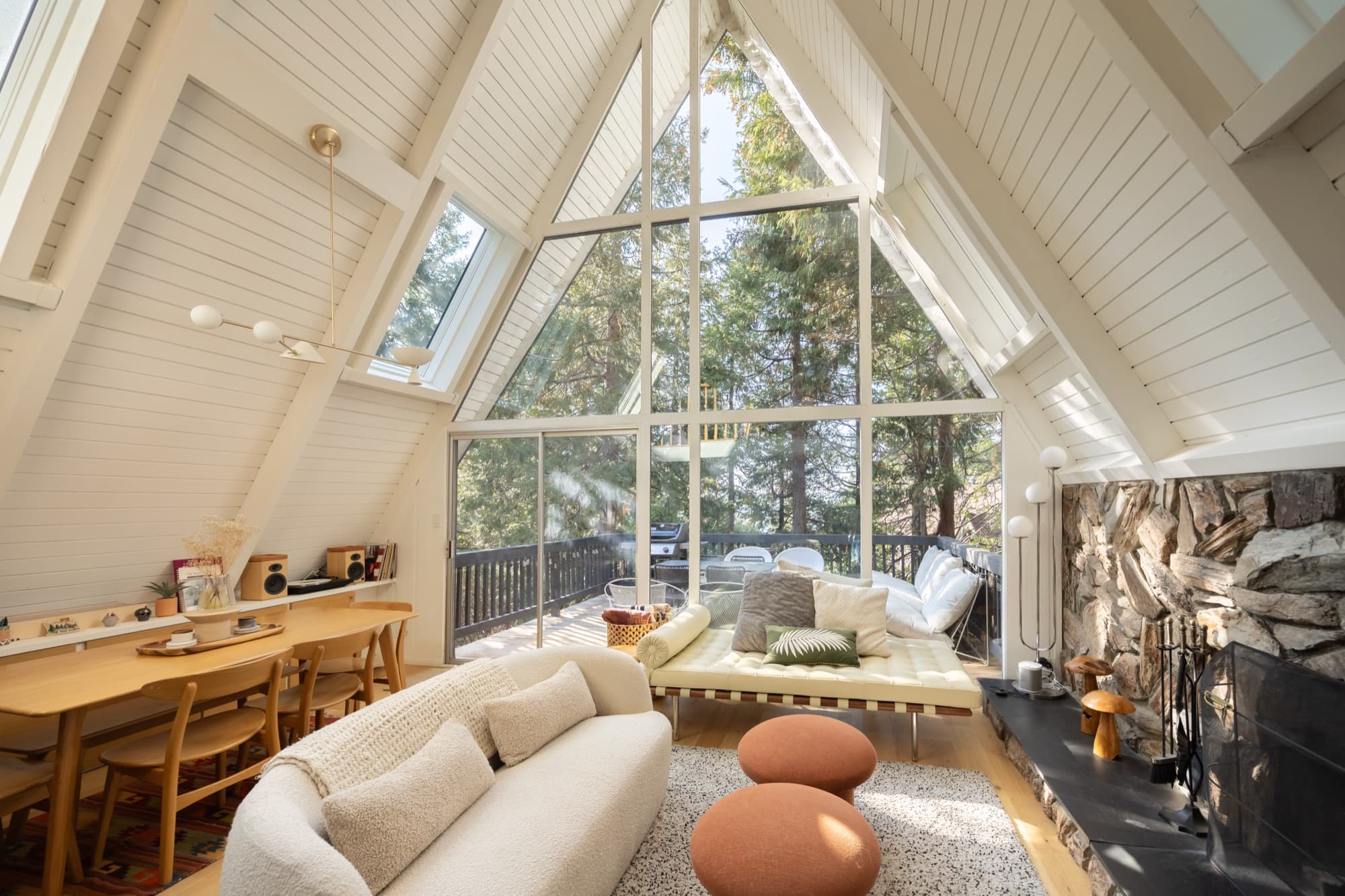 Living room with soaring A-frame ceiling, stone fireplace, cream sofas, and floor-to-ceiling windows